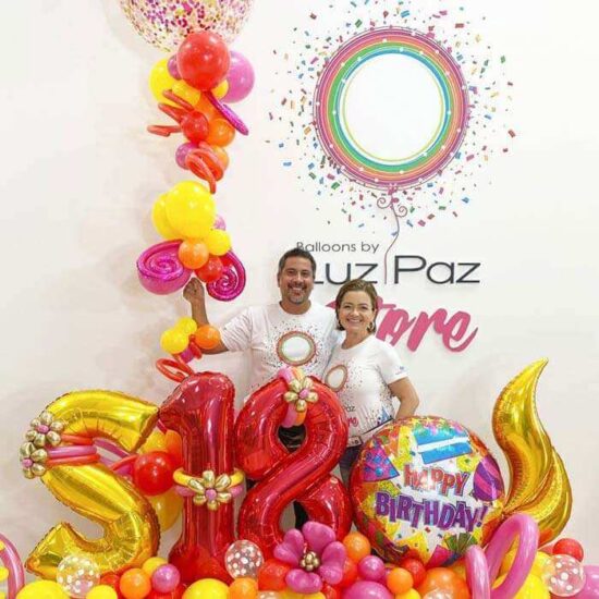 Luz Paz y Omar Bucio posando junto a maxi arreglo de globos con temática de cumpleaños.