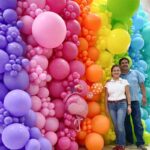 Luz y Omar posando junto a una pared de globos orgánica en colores llamativos.