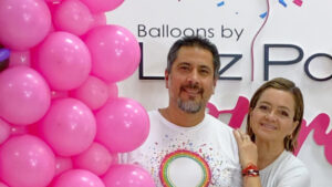 Luz Paz y Omar Bucio posando junto a una estructura de globos rosada.