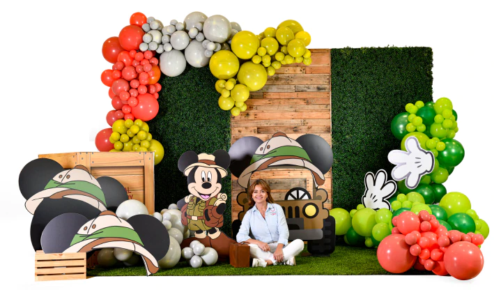 Luz Paz sentada junto guirnaldas con globos y pared decorativa con temática de Mickey Mouse en la jungla.