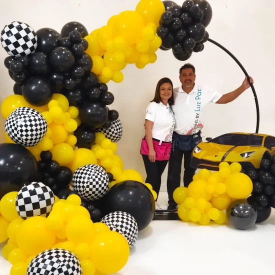 Luz Paz y Omar Bucio junto a decoración con globos con temática de auto de carrera.