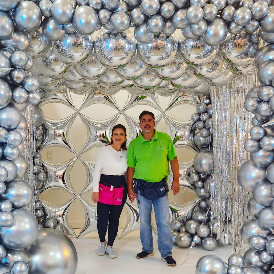 Imagen de Luz Paz y Omar Bucio junto a una estructura de gazebo en tonos plateados, decorada con globos, muy elegante y sofisticada.