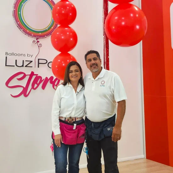 Luz Paz y Omar Bucio posando junto a una decoración con globos para techo a nivel intermedio.