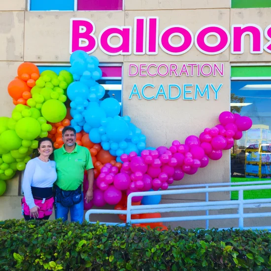 Luz Paz y Omar Bucio posando frente a la sede de Luz Paz Academy junto a una decoración con globos orgánica para ventanas.