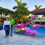Luz Paz y Omar Bucio junto a piscina con decoración con globos orgánica con temática de burbujas y flamingos.